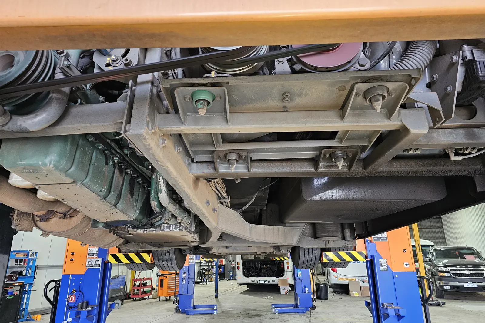 The underside of a bus raised on hoists, showing the chassis rails, air suspension and driveline