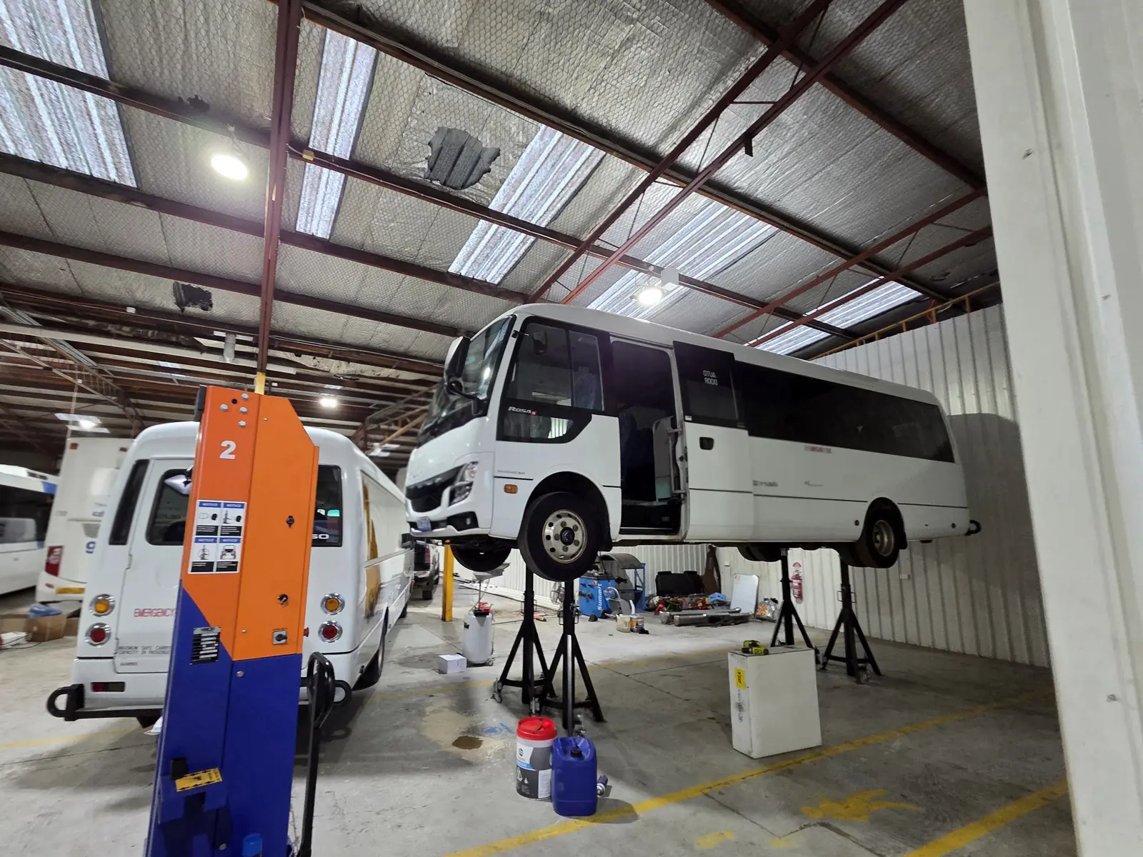 Two coaches raised on mobile column lifts in the workshop, with axle stands set underneath