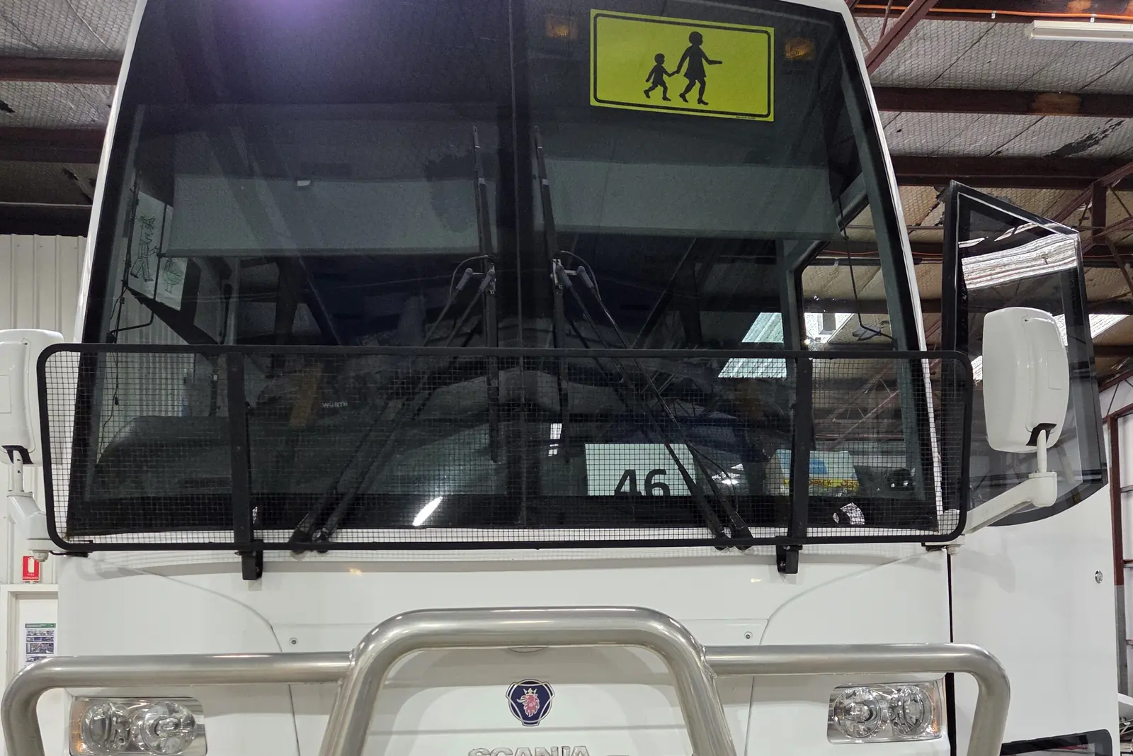 A school bus with a children-crossing sign in its windscreen, raised on the workshop hoists