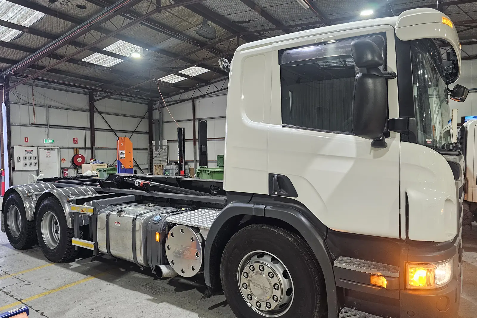 A white Scania prime mover with its headlights on, parked inside the workshop
