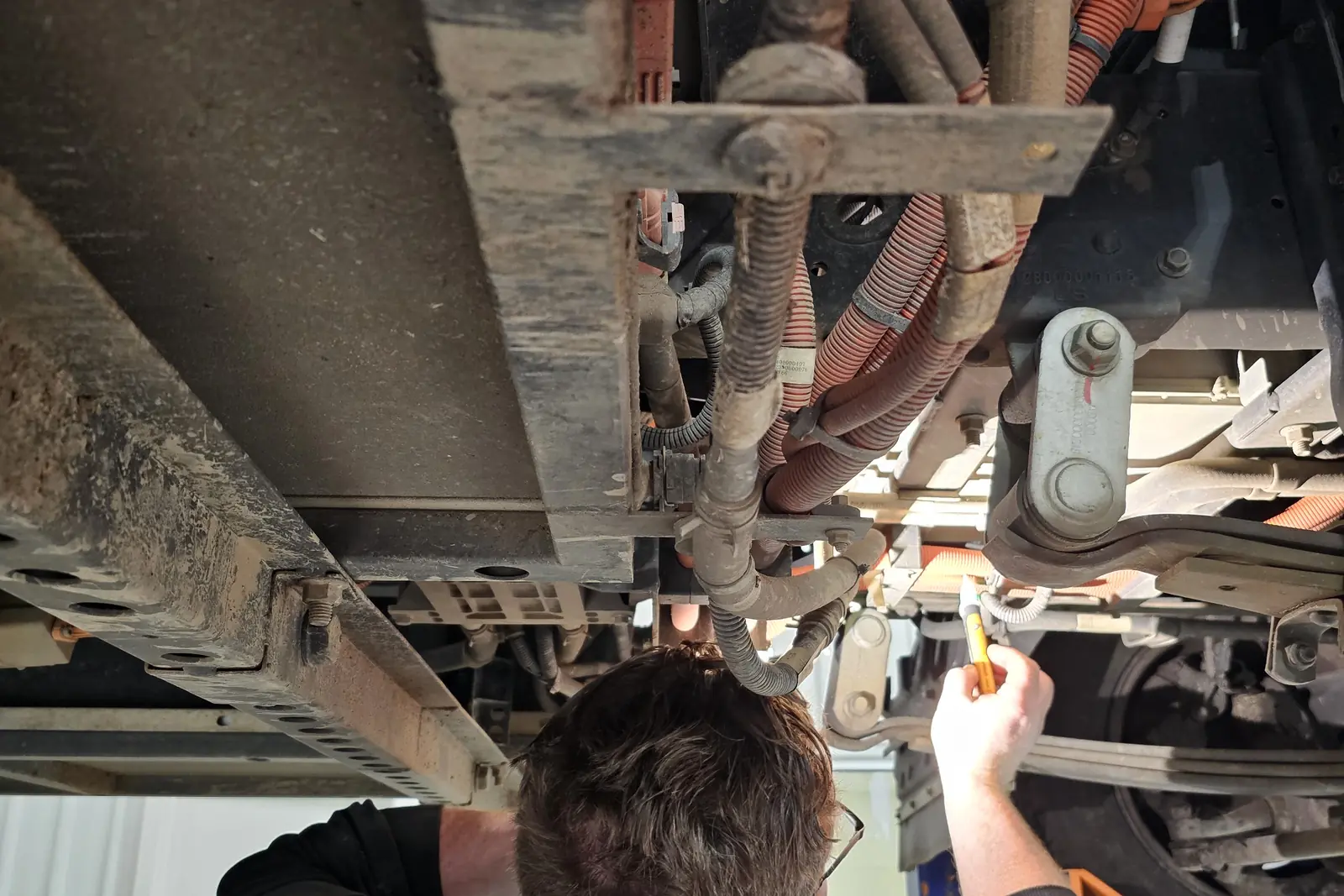 A technician using a torch to inspect the chassis of a raised truck