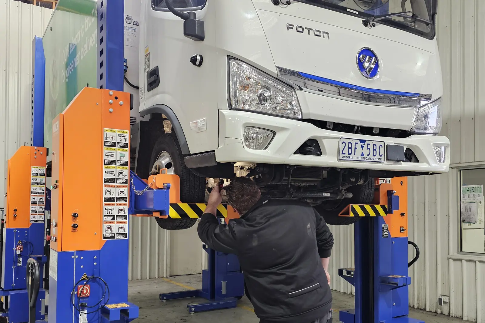 A technician working beneath a truck raised on mobile column lifts in the Wendouree workshop