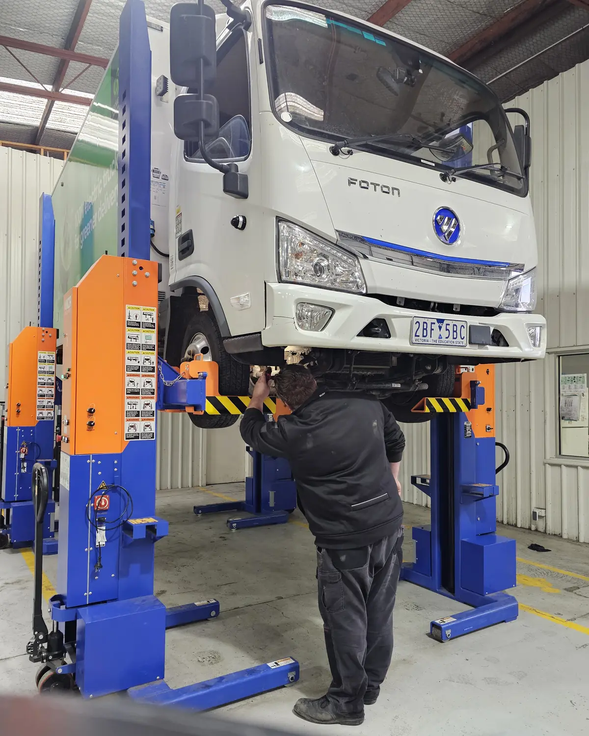 A technician working beneath a truck raised on mobile column lifts in the Wendouree workshop